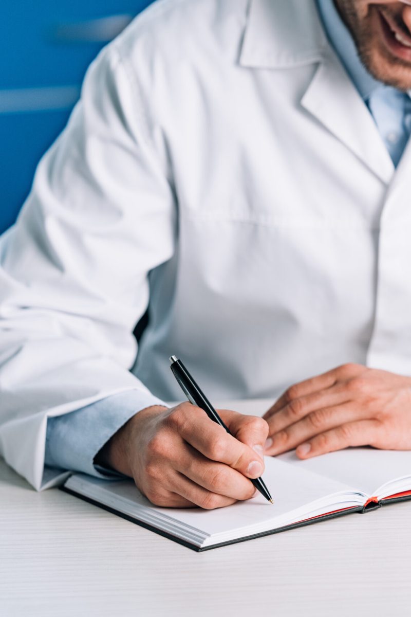 cropped view of happy doctor writing in notebook